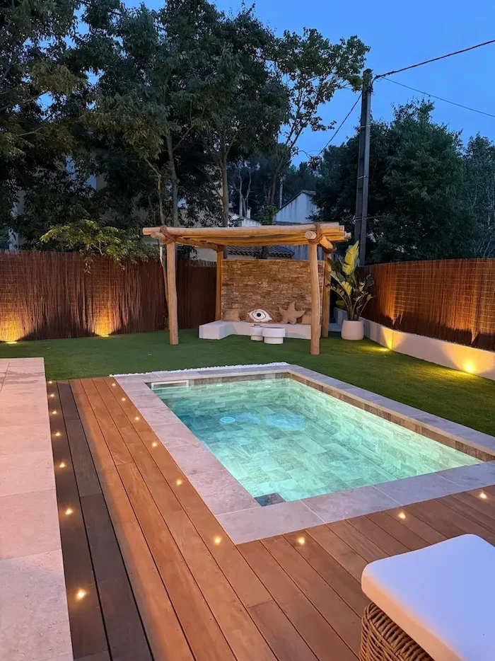 Petite piscine à la tombée du jour avec terrasse en bois et éclairage du jardin.